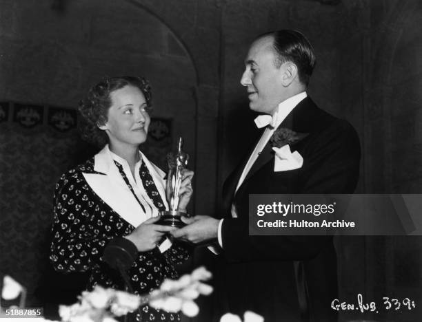 American actress Bette Davis and Canadian-born film producer Jack L. Warner , one of the founders of Warner Bros. Pictures, hold Davis's Oscar for...