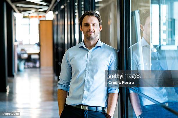 confident businessman leaning on glass wall in office - 30 34 years stock pictures, royalty-free photos & images