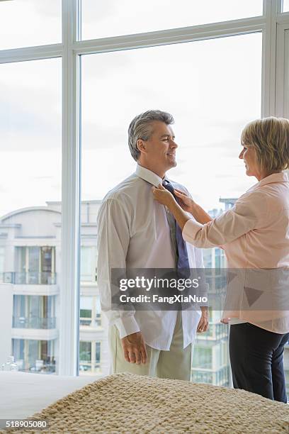 wife assisting husband with necktie - tied to bed stockfoto's en -beelden