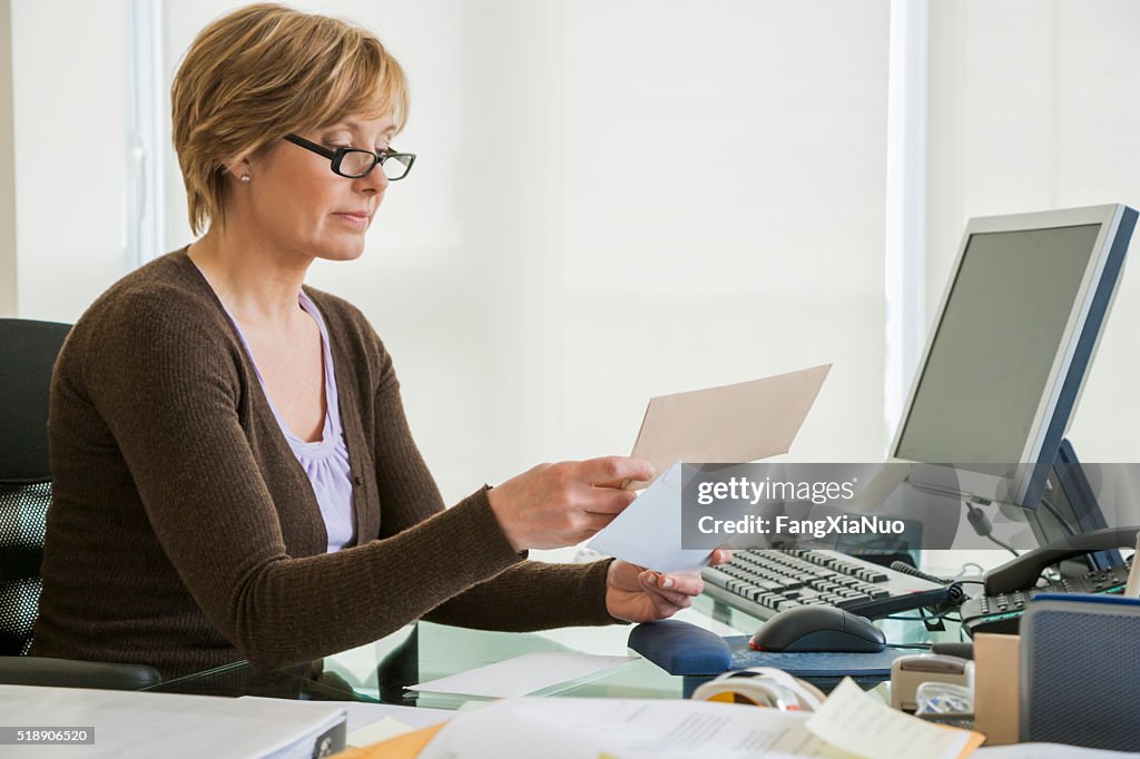 Middle-aged woman looking at bills at computer