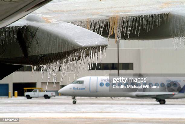 Icicles hang from the wing and engine of an aircraft while another jet prepares to leave at Columbus International Airport December 23, 2004 in...