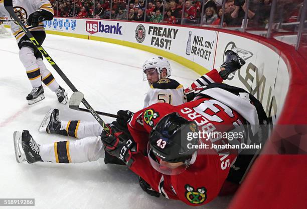 Viktor Svedberg of the Chicago Blackhawks falls over Ryan Spooner of the Boston Bruins in the corner as they chase the puck at the United Center on...