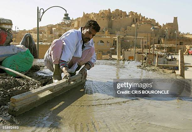 Construction worker levels concrete on the roof of a new building close to the ruins of the ancient fortification of Shali, located in the center of...