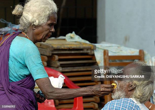 An elderly Indian lady feeds her disabled husband in a relief camp for victims of tidal waves in the Santhome Church in Madras, 27 December 2004. The...