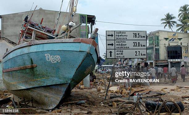 Sri Lankan residents walk past a fishing boat marooned on a road after a massive tidal wave struck the southern district of Galle, 27 December 2004....