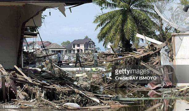 Passersby walk amid debris of destroyed buildings, 27 December 2004 in Banda Aceh, after tidal waves hit the region. The carnage suffered when...