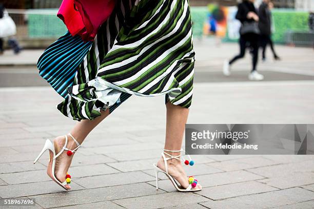Showgoer wears quirky green-striped skirt and white heels with pompoms at the Mary Katrantzou show at 1 Granary Square during London Fashion Week...