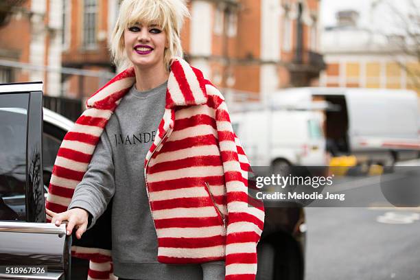 French model Celine Bouly enters her car and wears fuchsia lipstick, cat-eye makeup, a red and white striped fur coat, and J.W. Anderson gray...