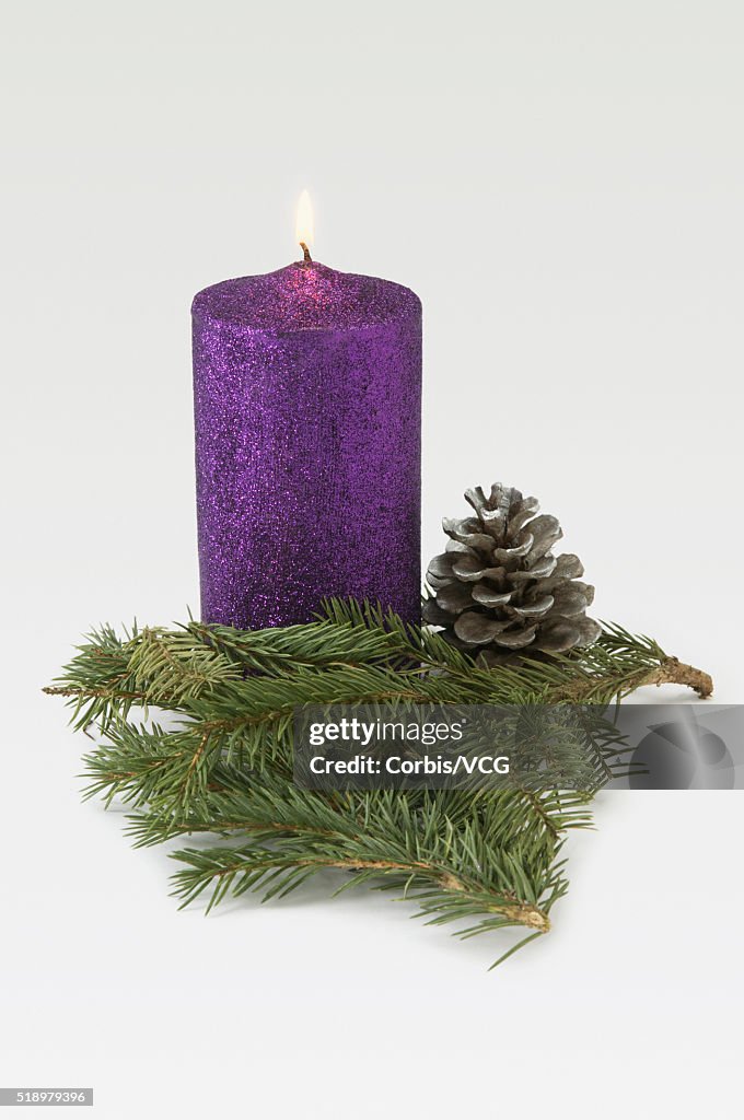 Detail view of a Christmas candle decorated with evergreen branches and a pinecone