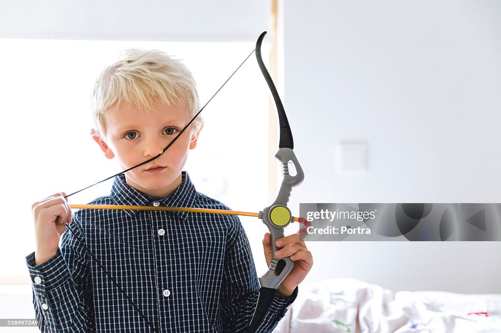 Boy holding toy bow and arrow at home