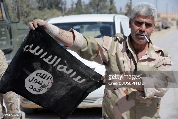 Syrian soldier displays on April 4, 2016 an Islamic State group flag after Syrian troops regained control the previous day of al-Qaryatain, a town in...