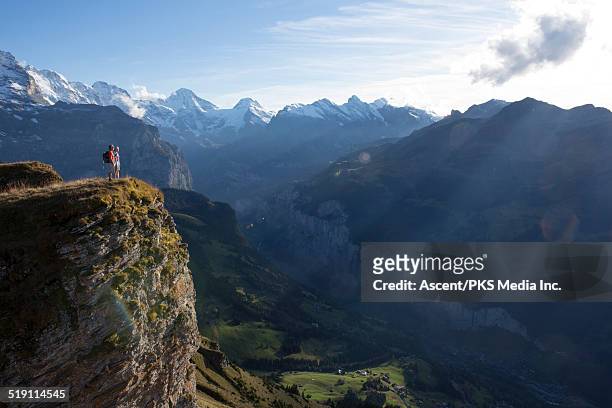 distant couple look out across mountain valley - steilküste stock-fotos und bilder