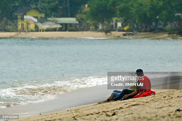 Couple of tourists sit on the beach in the southwestern coastal town of Galle 04 January 2005. Heavy rains slowed relief operations in Sri Lanka's...