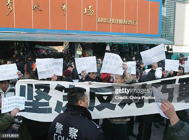 Vendors protest with a slogan reading "Strongly oppose the robbery" under watch of police, in front of the old Xiushui Market on January 4, 2005 in...