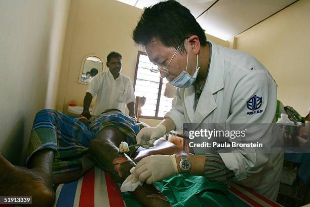 Dr. Kim Hyun Min , with the Korean Disaster Medical Assistance team , treats a tsunami earthquake victim's wounds at the District hospital of...