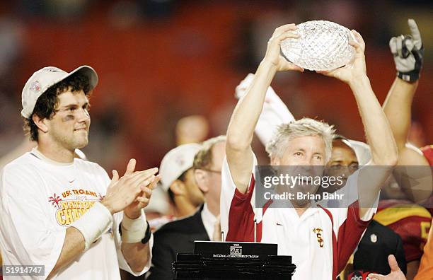 Head coach Pete Carroll of the USC Trojans holds up the championship trophy as quarterback Matt Leinart celebrates after defeating the Oklahoma...