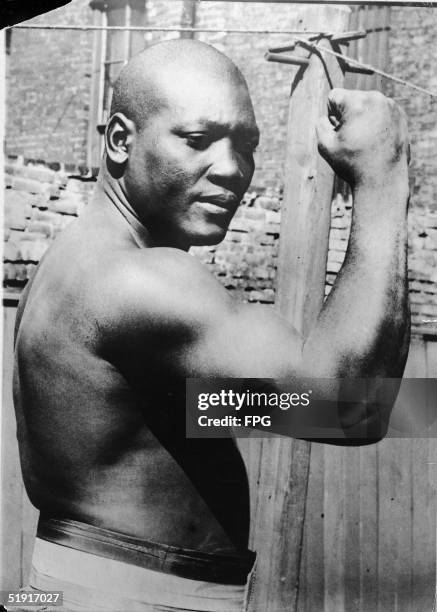 American boxer Jack Johnson , the world heavyweight champion, wears his championship belt and flexes his bicep outside his home in Chicago, Illinois,...