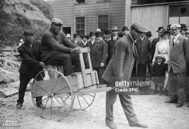 American boxer Jack Johnson , the world heavyweight champion, rides in a cart past spectators on the street, San Francisco, California, early 1910s.