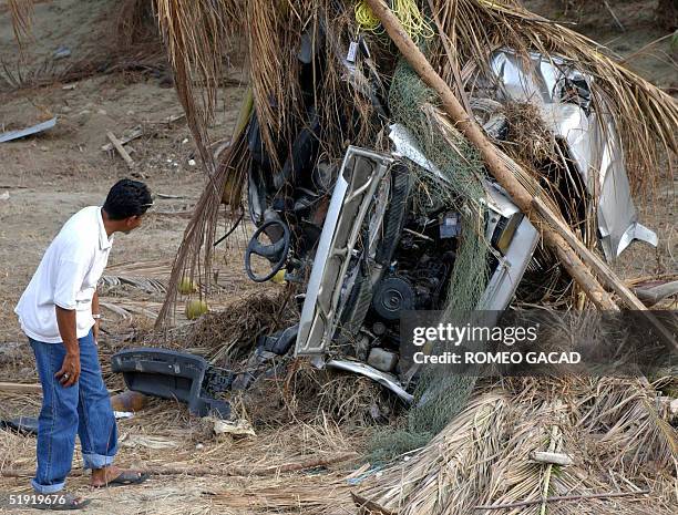 Man examines a vehicle twisted around a coconut tree in Khao Lak, Phang Nga province 06 January 2005 after a killer tsunami engulfed the area....