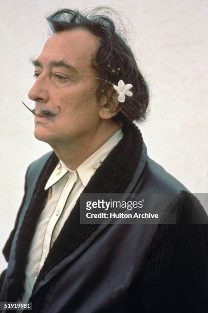Three-quarter profile portrait of Spanish surrealist painter Salvador Dali dressed in a smoking jacket with a flower in his hair, early 1980s.