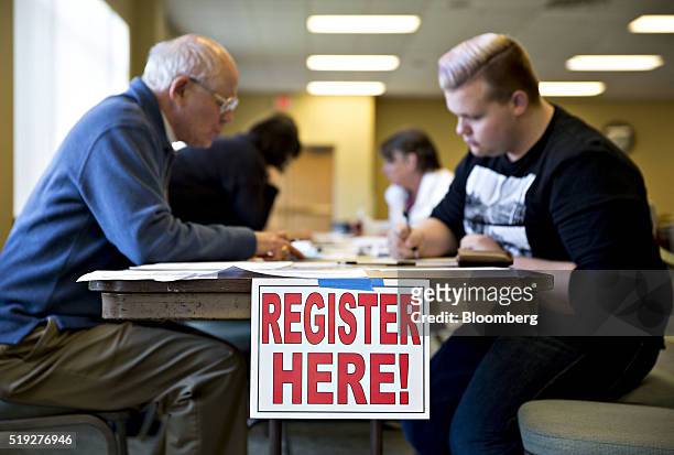 Register Here" sign hangs on a table as a resident fills out paperwork at a polling location during the presidential primary vote in Waukesha,...