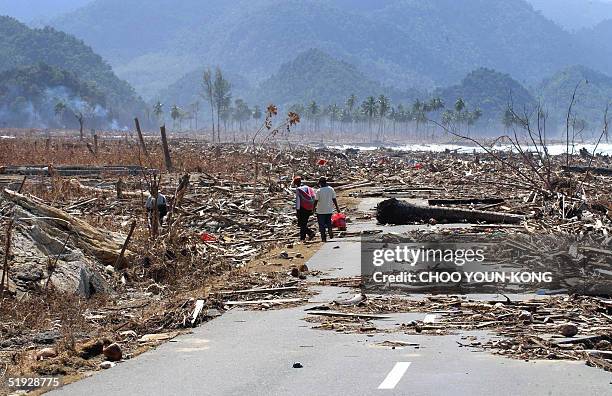 Two Indonesian refugees walk down a road covered with debris leftover from the tsunami disaster as they return to look for their homes in the west...