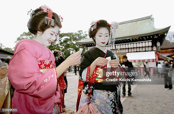 Two Japanese Maikos prepare to tie paper fortunes to a tree on the first business day of the new year at Yasaka Jinja on January 9, 2005 in Kyoto,...