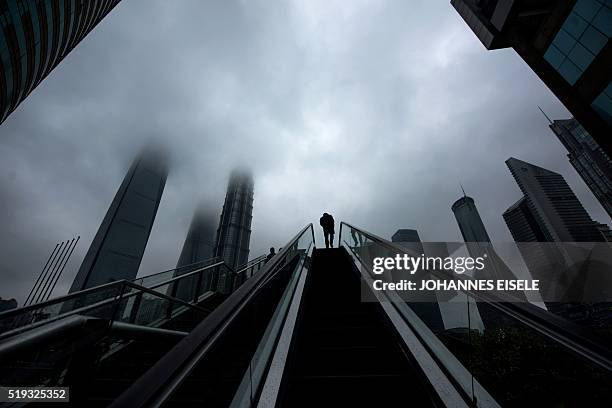 Man rides an escalator in front of high rise buildings in the financial district Lujiazui in Shanghai on April 6, 2016. / AFP / JOHANNES EISELE