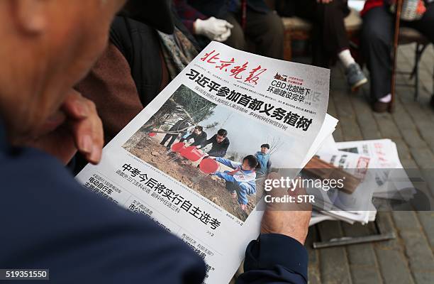 Man reads a newspaper featuring a front page photo of Chinese leaders including President Xi Jinping attending a tree planting ceremony, at a news...