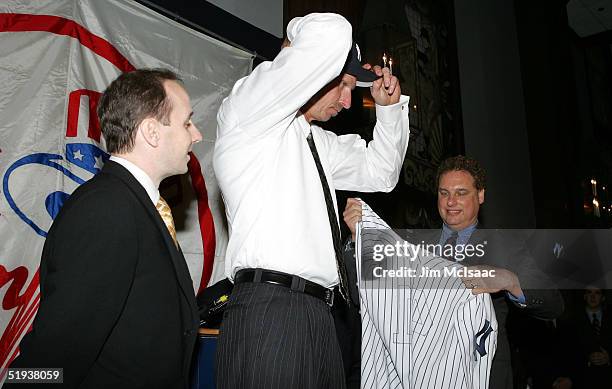 Newest member of the New York Yankees, Randy Johnson , tries on his cap as team president Randy Levine holds his jersey while general manager Brian...