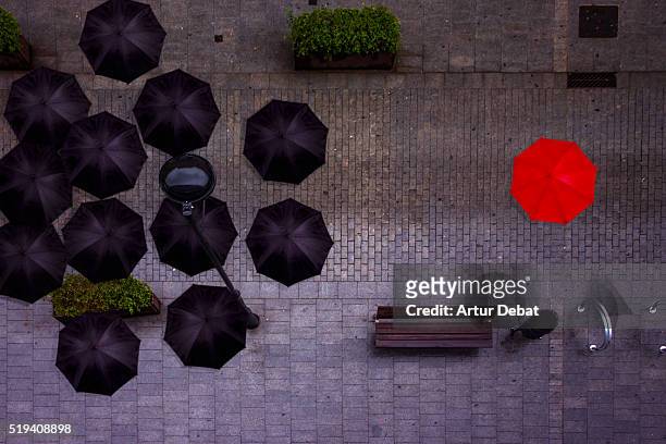 view from above of a man with red umbrella stands out from the rest of black umbrellas in a rainy and dark day in the city. - vanguardians - fotografias e filmes do acervo