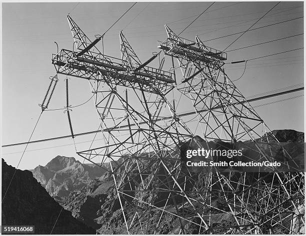 Black and white photograph of transmission line towers on a cliff face, both towers in the photograph were constructed angled away from the cliff...