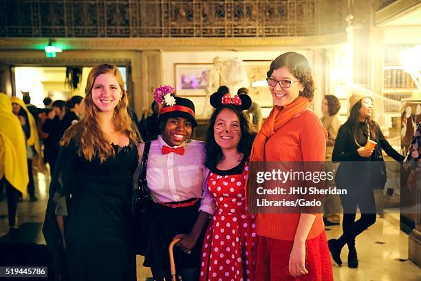 Four female college students are posing and smiling, the girl on the far left is wearing a black dress, the next girl is dressed as Mary Poppins and...