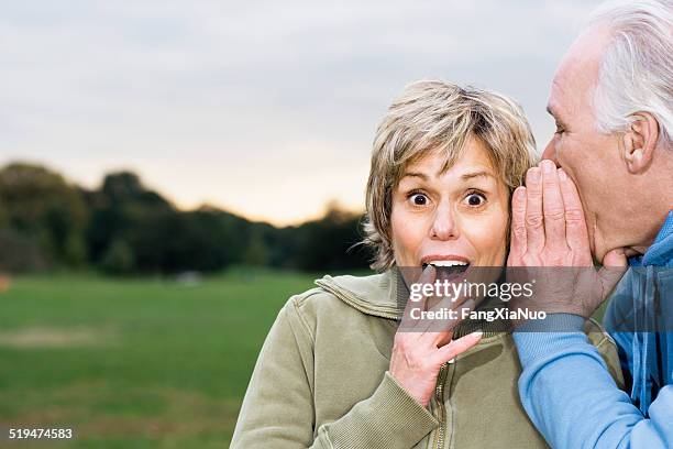 senior man telling woman secret, outdoors, portrait - whispering stock pictures, royalty-free photos & images