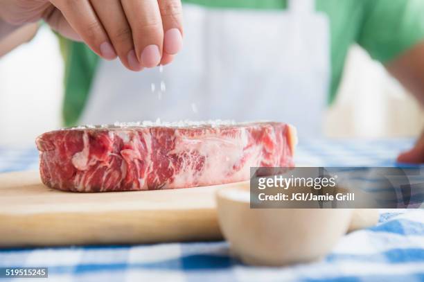 close up of mixed race man sprinkling salt on steak - sales occupation fotografías e imágenes de stock