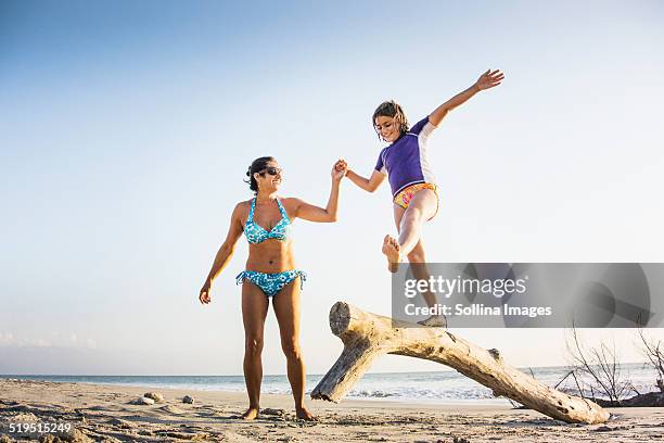 mother and daughter playing on log on beach - hot mexican girls fotografías e imágenes de stock