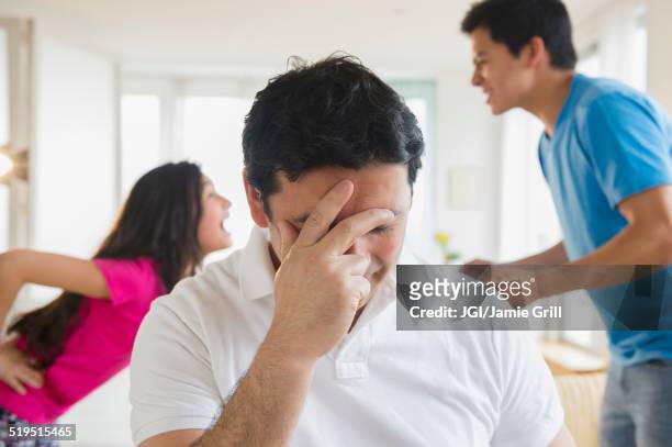 hispanic father covering his face as children fight behind him - sibling argument stock pictures, royalty-free photos & images