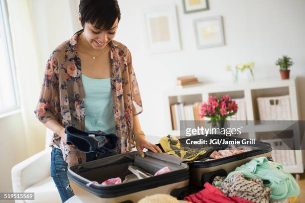 mixed race woman packing suitcase for vacation - suitcase packing stockfoto's en -beelden
