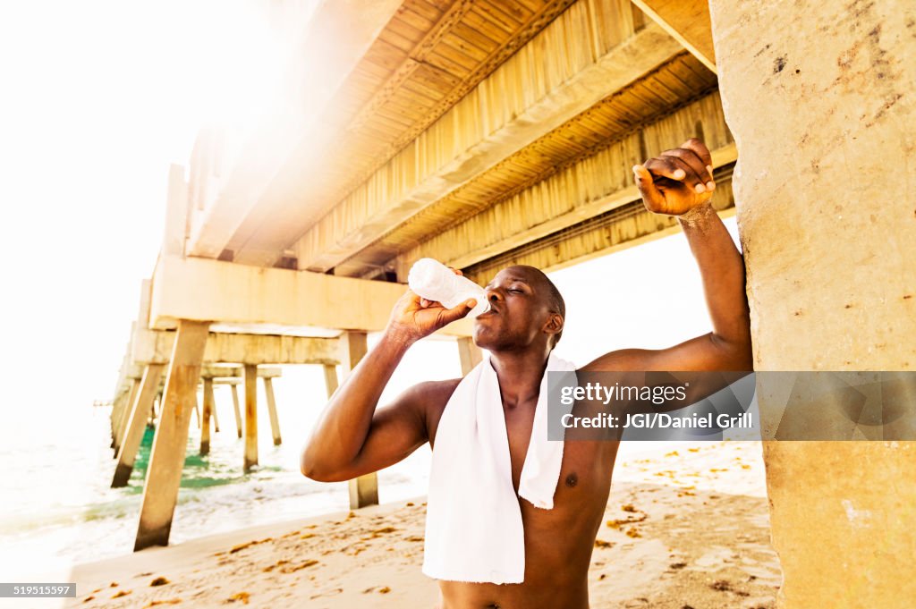 Mixed race man drinking water under pier