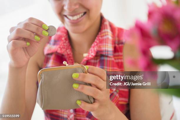 mixed race woman putting coin into purse - lady wallet stock-fotos und bilder