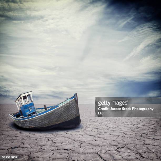 dilapidated boat on dry cracked river bed - paisaje árido fotografías e imágenes de stock