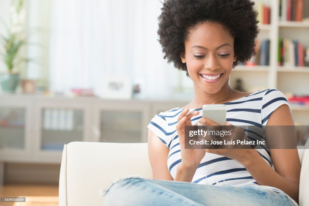 African American woman using cell phone on sofa