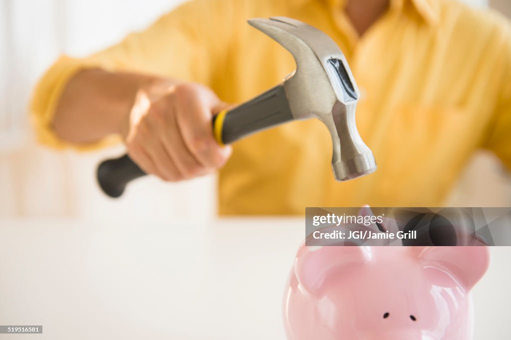 Close up of mixed race man holding hammer over piggy bank