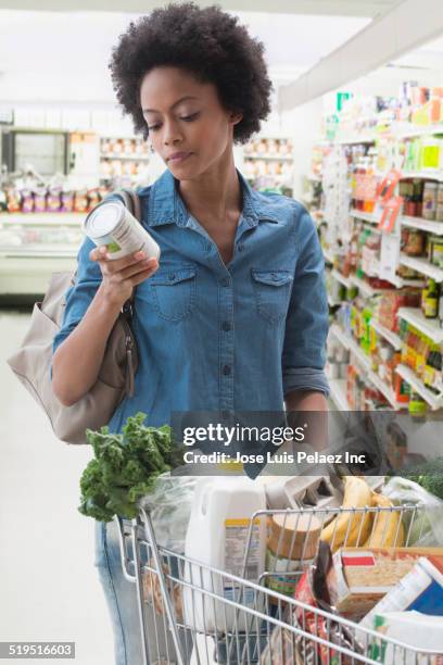 african american woman shopping in grocery store - frau einkaufswagen ernst stock-fotos und bilder