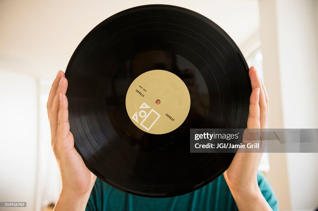 Mixed race man obscuring face with vinyl record