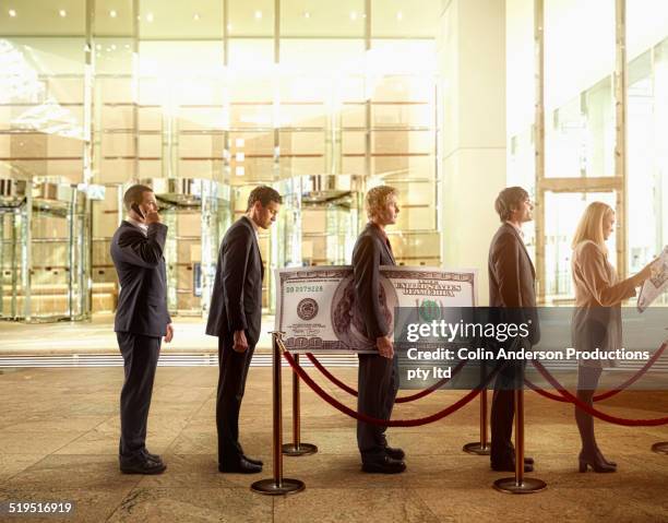 businessman holding large hundred dollar bill in bank line - men and women in a large group listening stock-fotos und bilder