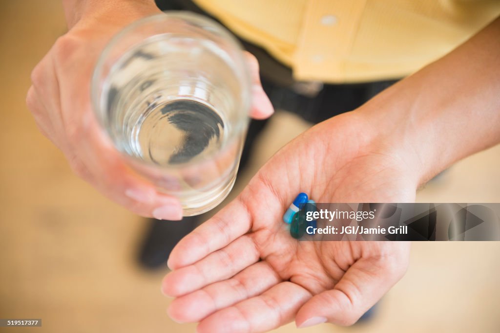 Close up of mixed race man holding medicine and glass of water