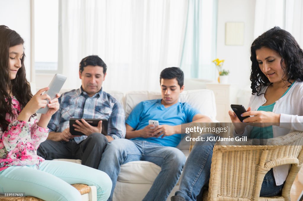 Hispanic family using cell phones and digital tablets in living room