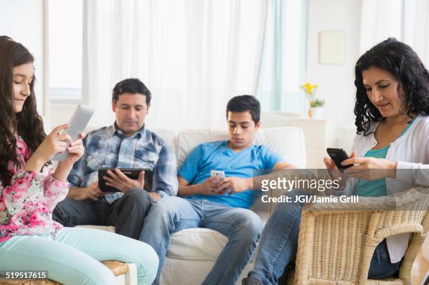 hispanic family using cell phones and digital tablets in living room - mature man using phone tablet stock pictures, royalty-free photos & images