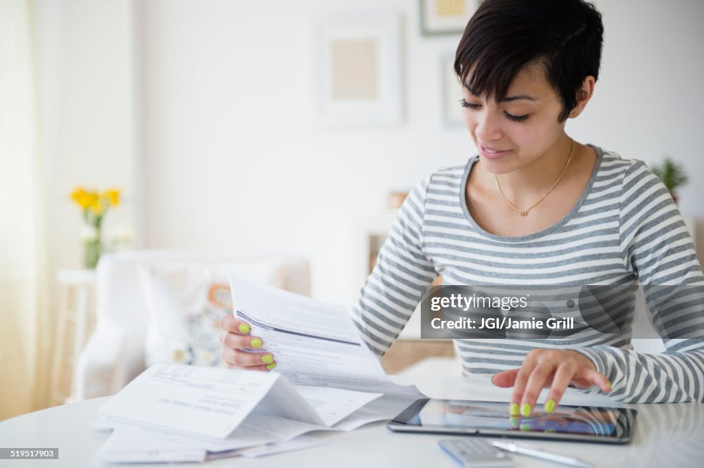 Mixed race woman paying bills on digital tablet